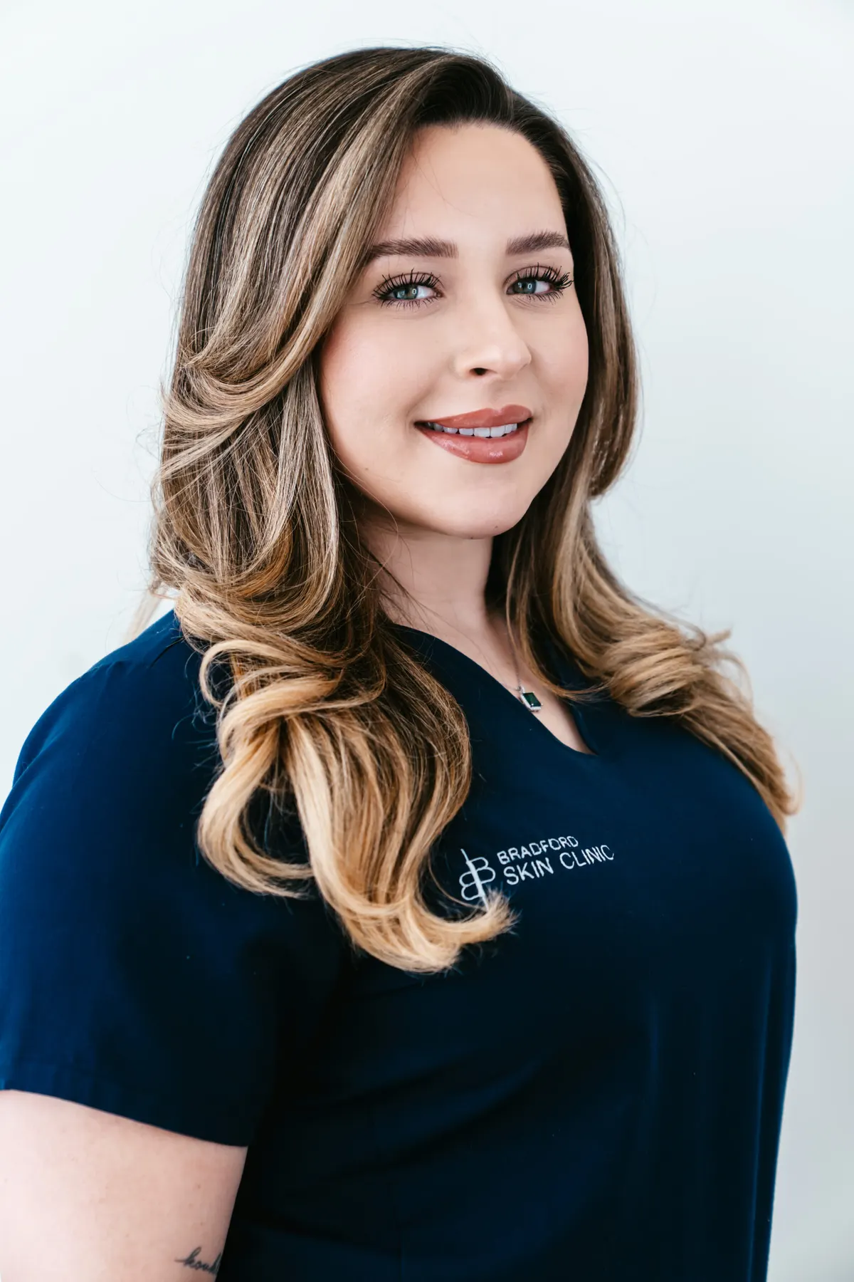 A member of the clinic team photographed in Bradford Skin Clinic navy scrubs against a plain studio background.