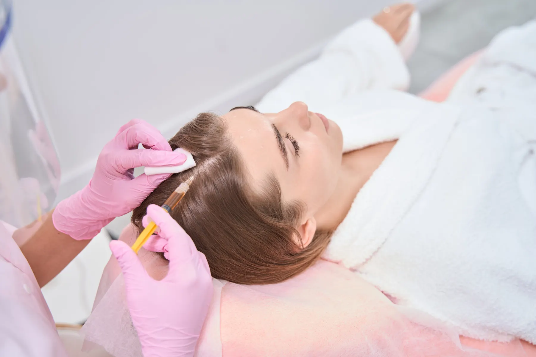A clinician in sterile gloves passing a microneedling device across a client's cheek