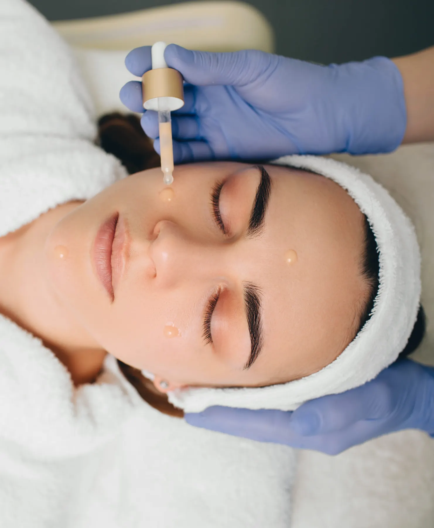 A client lying back in profile with a white treatment mask applied across her face and a white headband.