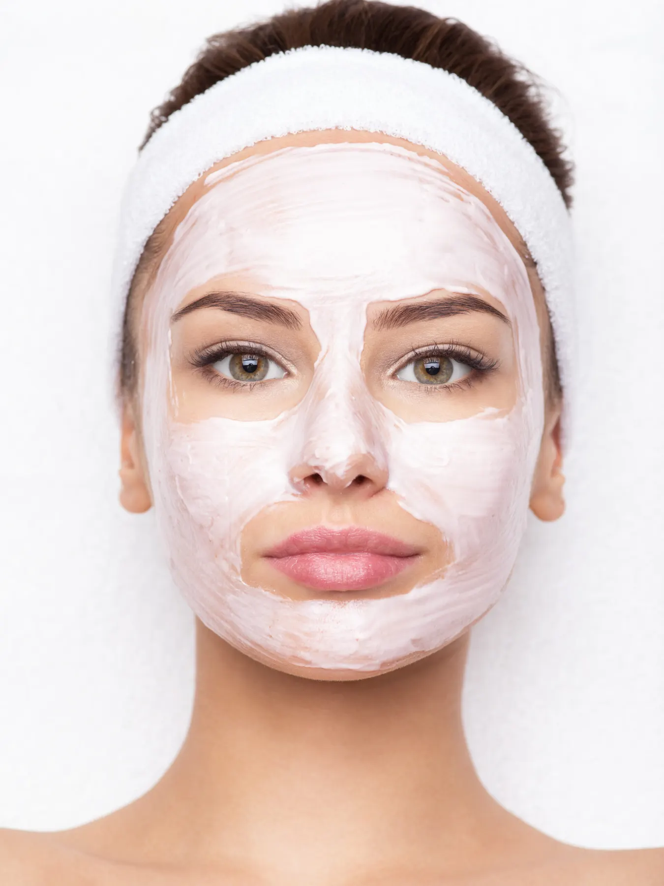 A client facing the camera with a white treatment mask applied evenly across her face and a white headband.
