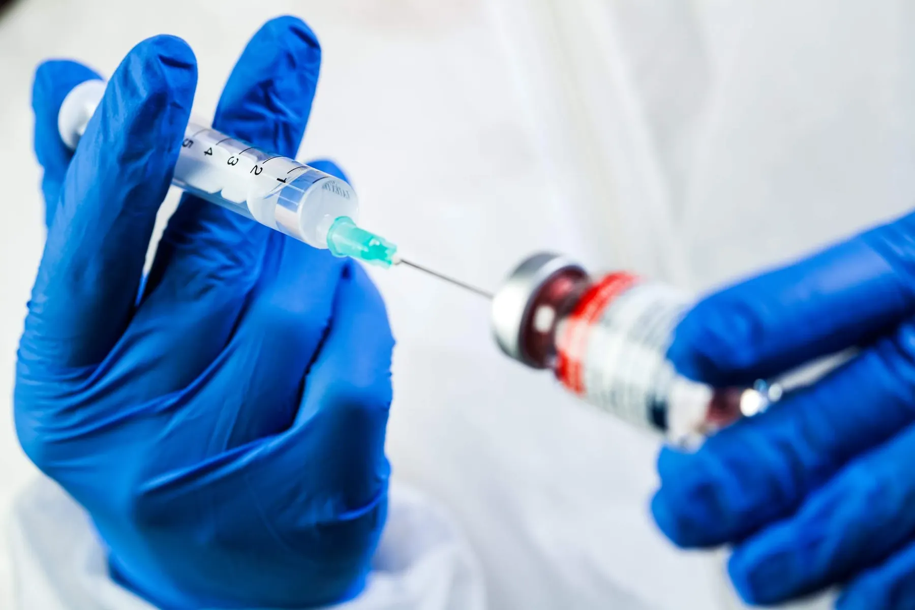 A gloved hand drawing product up into a syringe.