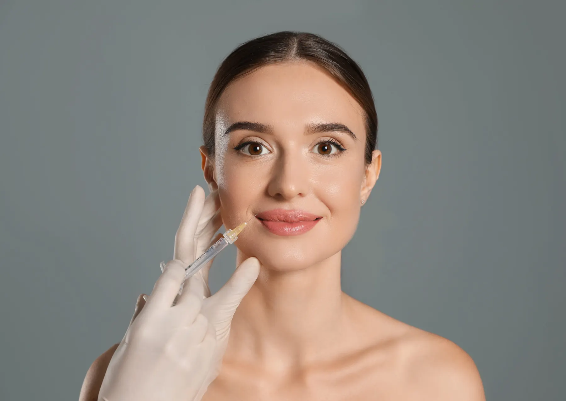 A gloved hand injecting dermal filler into a lip.