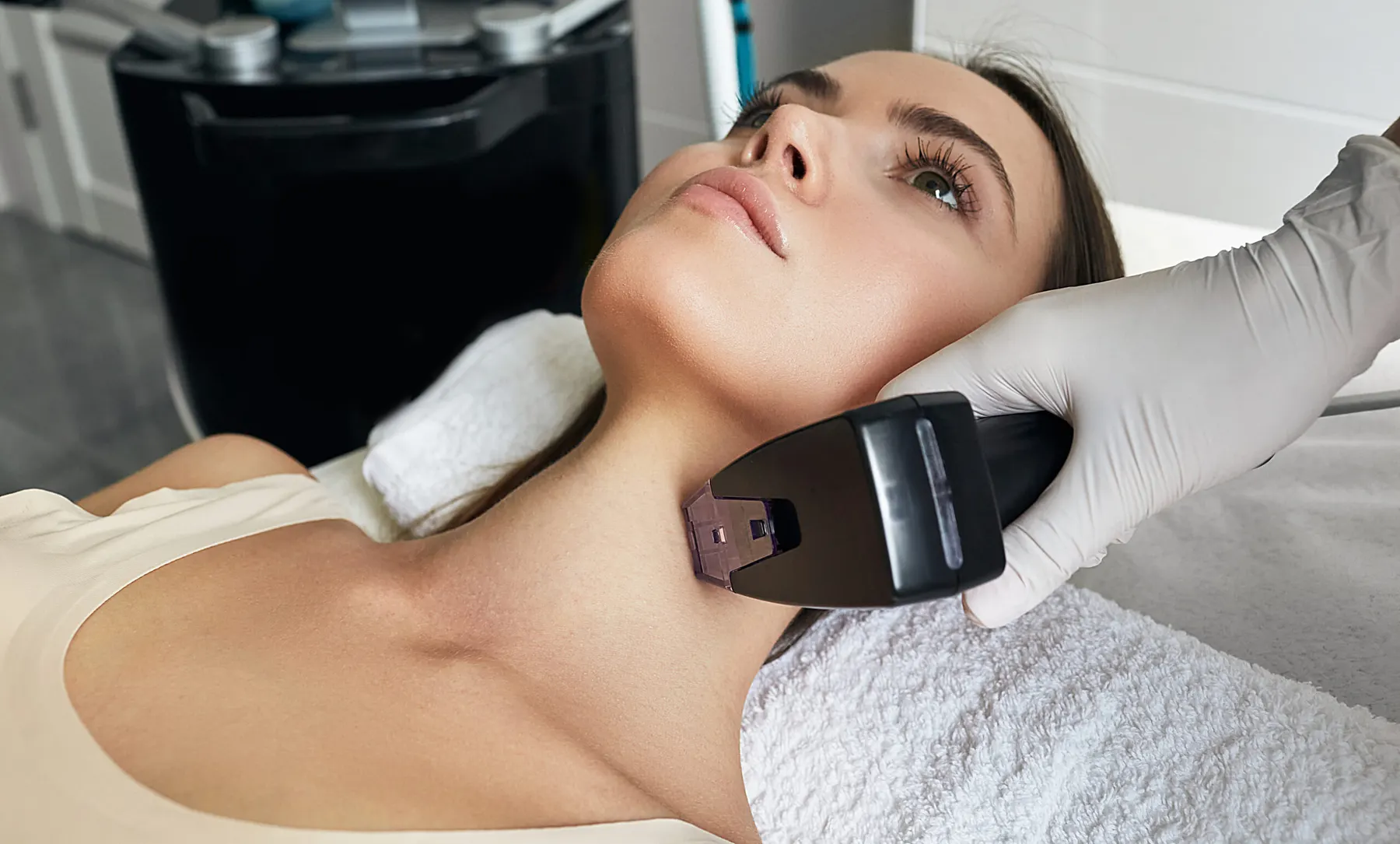 A gloved hand pressing a rectangular treatment applicator against the side of a client neck.