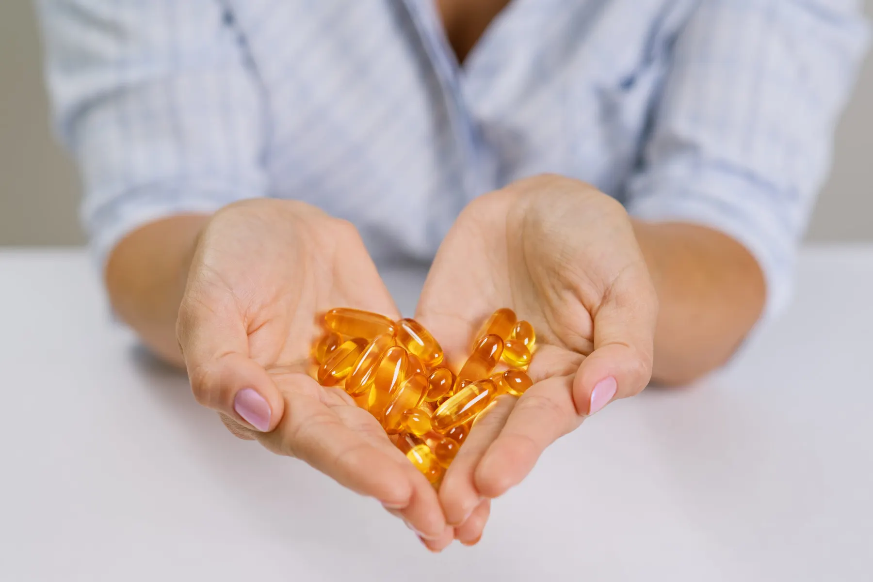 Two cupped hands holding a small heap of amber supplement capsules arranged in a heart shape.
