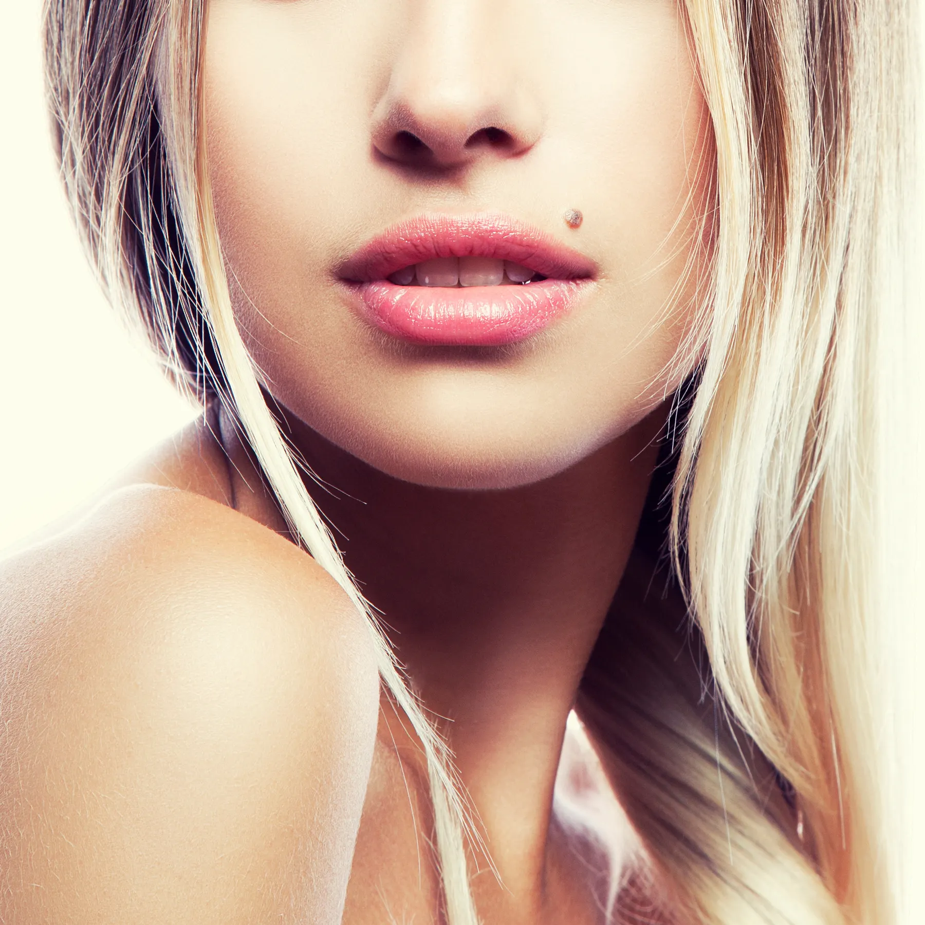 A close-up of a blonde woman's face and hair, with a small mole visible on her cheek.