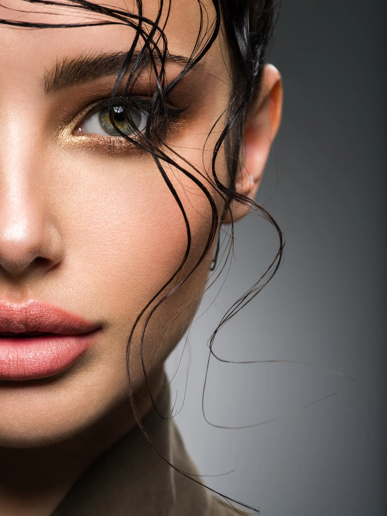 Extreme close-up of one half of a face with gold eye makeup and loose strands of dark hair