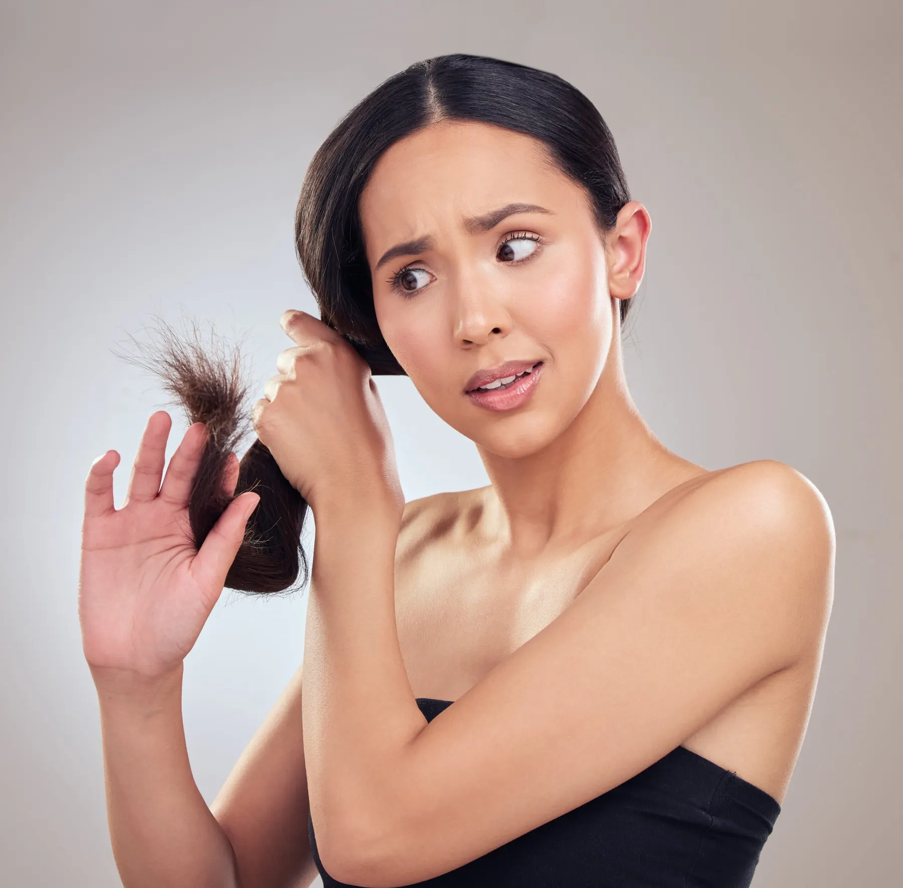 A woman holding up a thin, frayed lock of her own hair and looking at it with concern