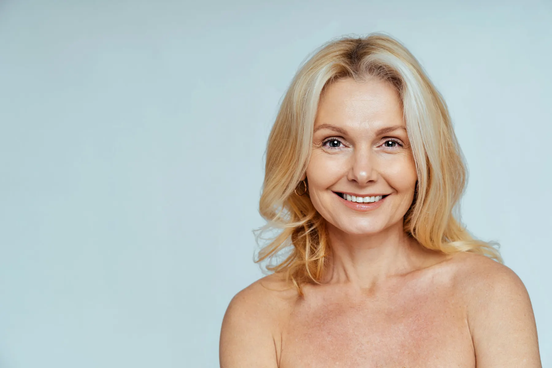 A smiling woman with shoulder-length blonde hair photographed against a plain pale background.